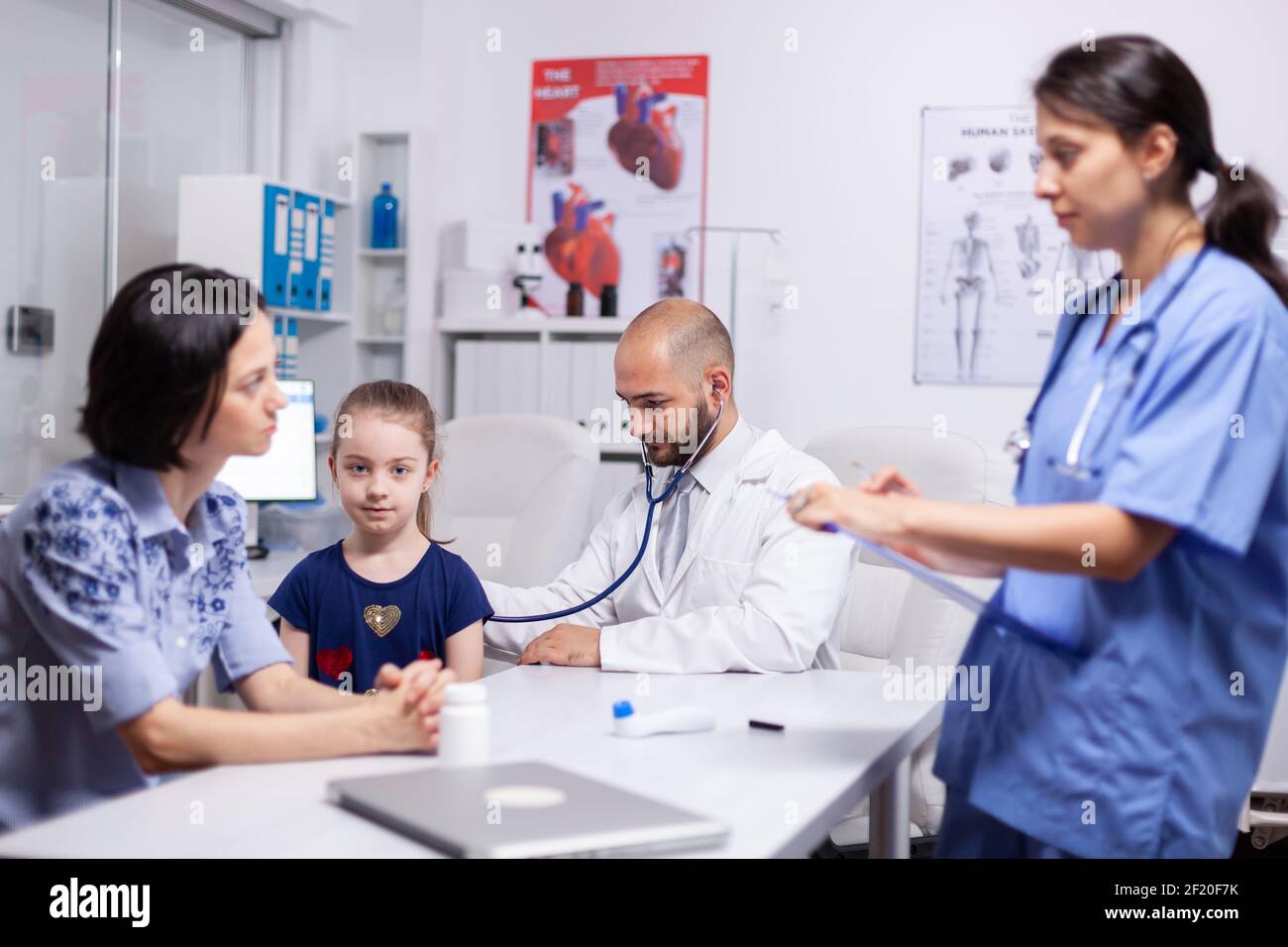 Doctor pediatry checking evolution of flu using stethoscope and nurse writing disease symptoms. Healthcare practitioner in medicine providing professional treatment services in hospital clinic. Stock Photo