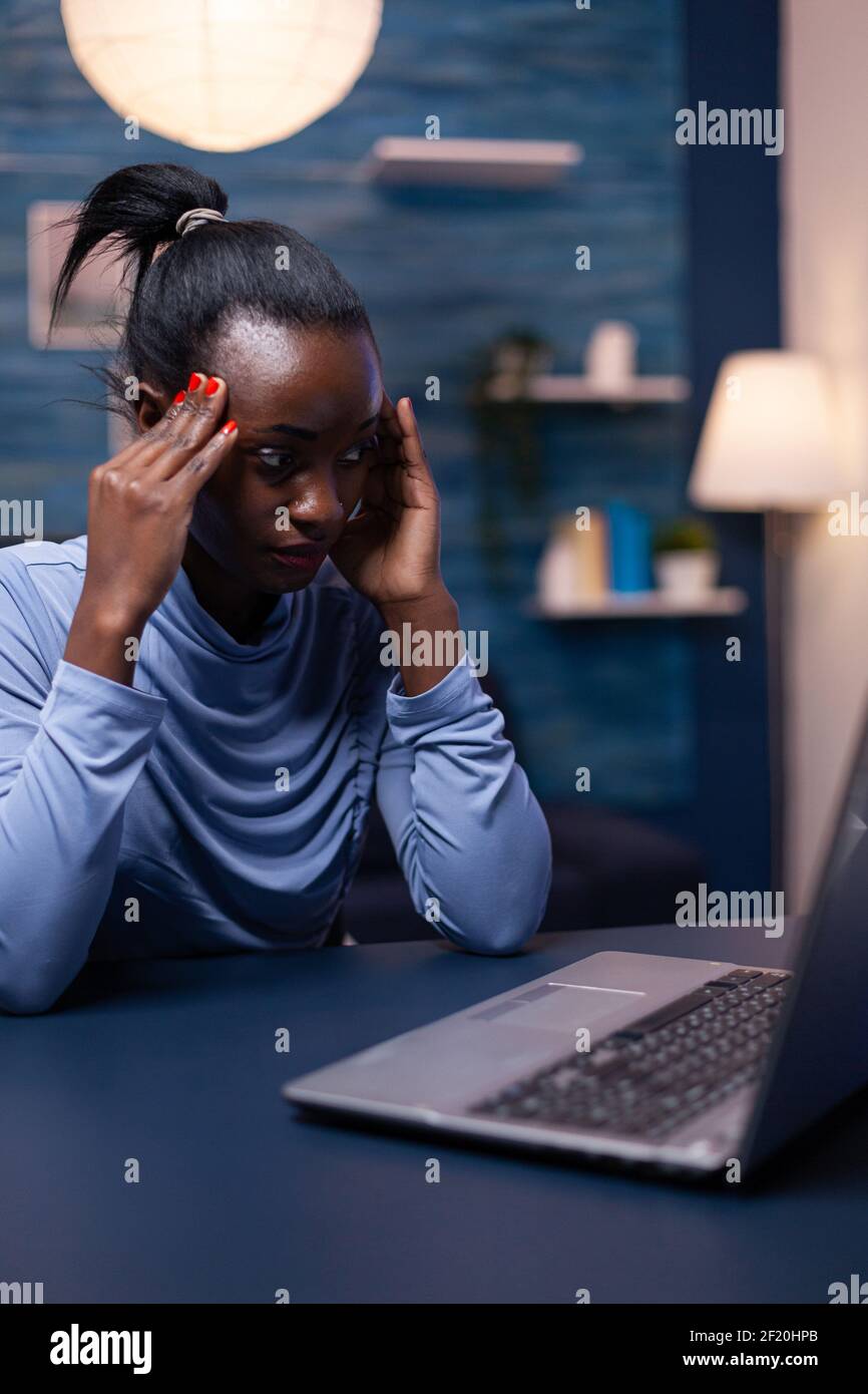 Overworked african business woman having a headache while working late in  the night from home office. Tired focused employee using modern technology  network wireless doing overtime Stock Photo - Alamy