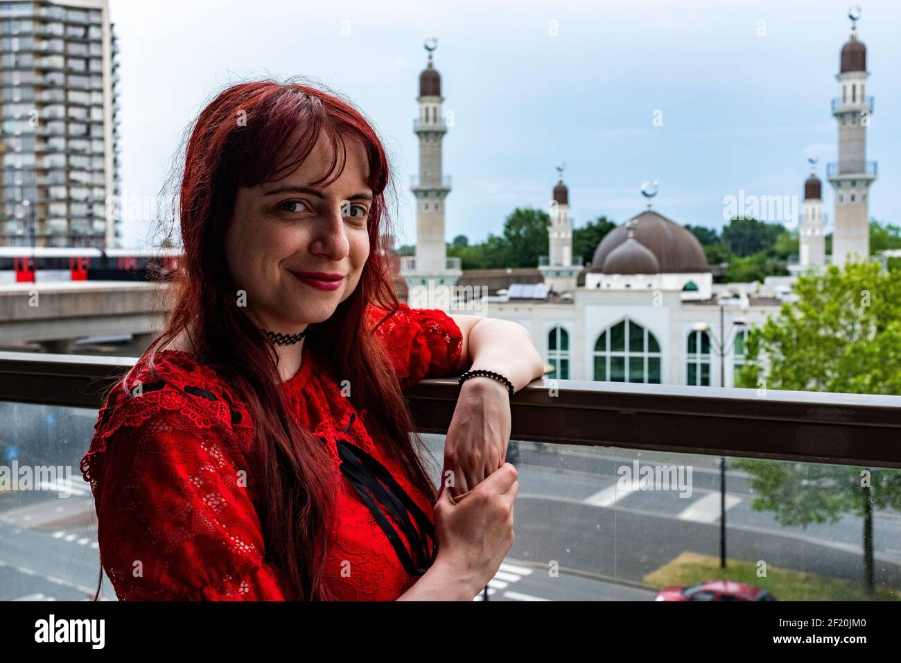 Amsterdam, Netherlands. Young, redhaired woman leaning over the fence of her balcony, with view to a local Islamic Mosque. These Islamitic prayer and worship houses are en masse erected in North-East Europe and often funded by conservative Islamitic nations, like Saoudi-Arabia and Iran. Stock Photo