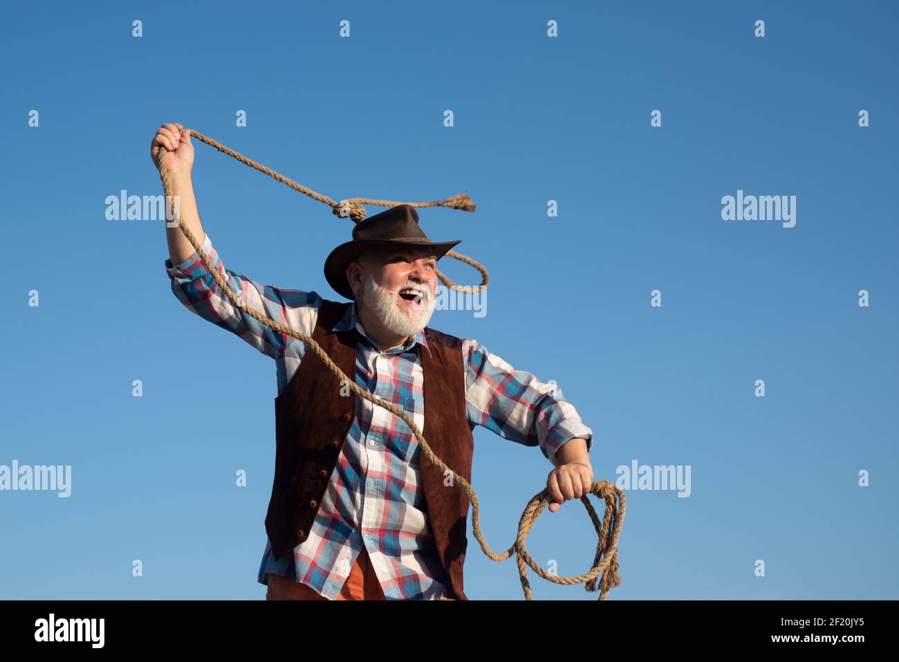 Senior western cowboy throwing lasso rope. Bearded wild west man with
