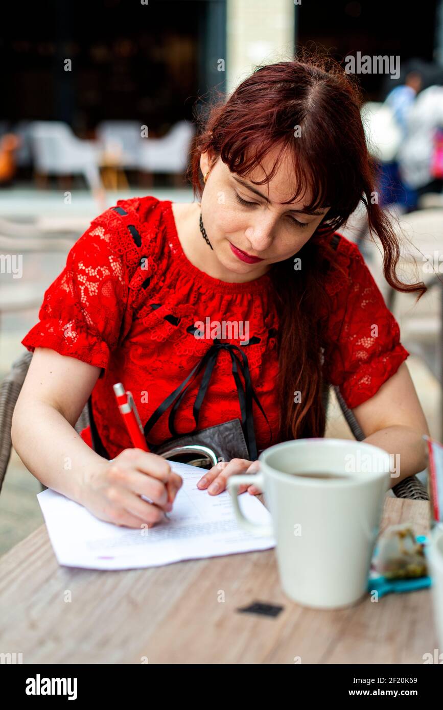 Amsterdam, Netherlands. Young, redhaired woman drinking a cup of tea on a sunny outside terrace inside a shopping mall. Stock Photo