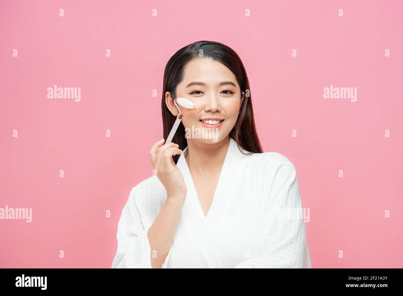 Beauty face care. Woman doing face massage with rose quartz face roller for spa skin care treatment at home Stock Photo