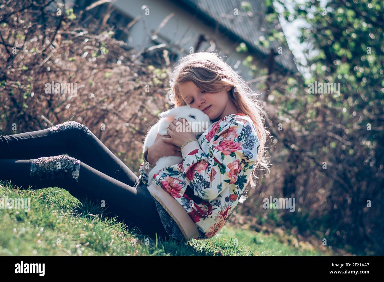 little girl sitting in the grass and hugging a white fluffy rabbit pet ...