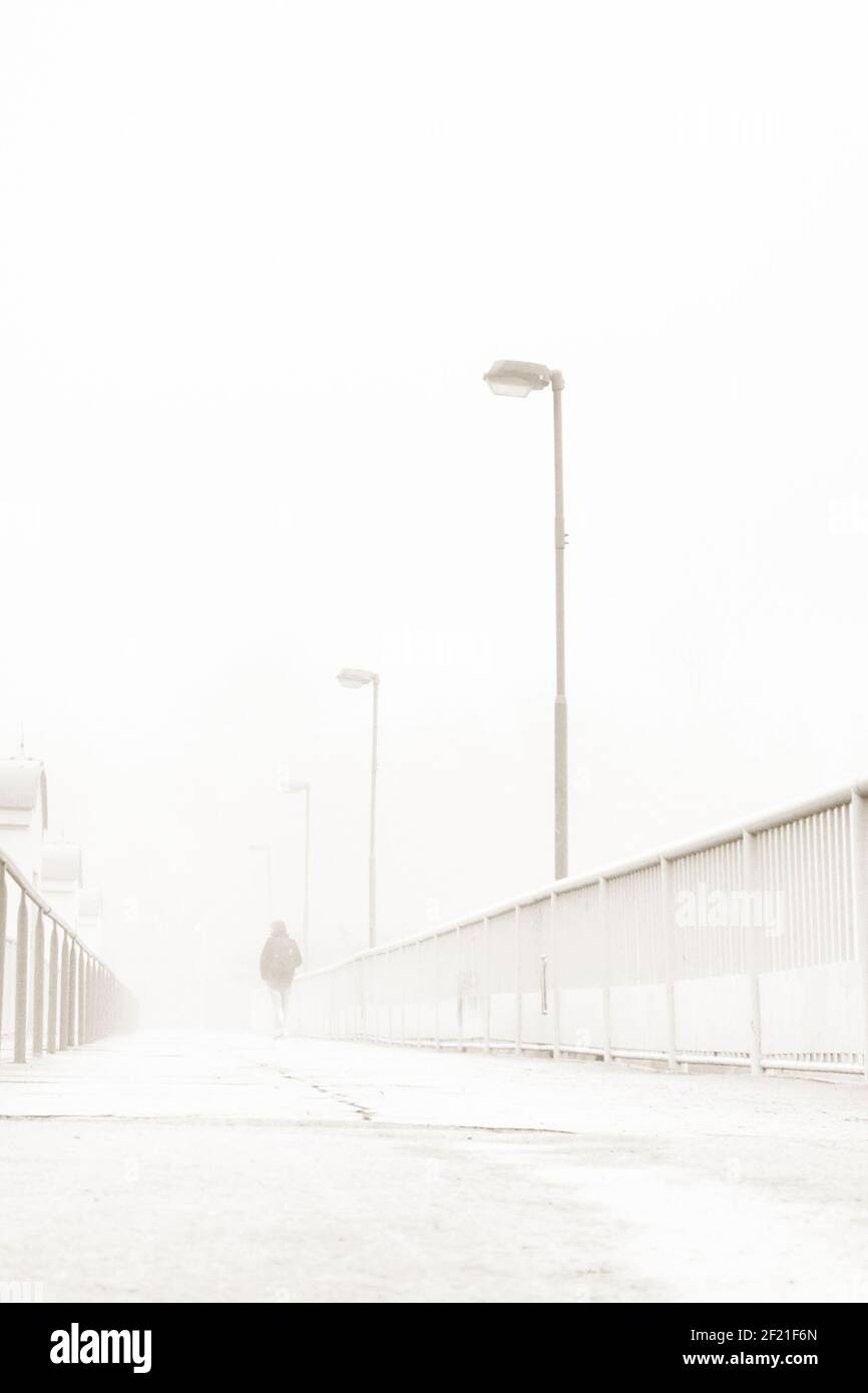 mysterious figure walking away along a bridge in a foggy day Stock Photo