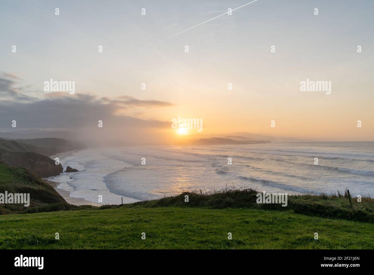 Tall green grassy cliffs drop down to the ocean coast in northern Spain at sunset Stock Photo