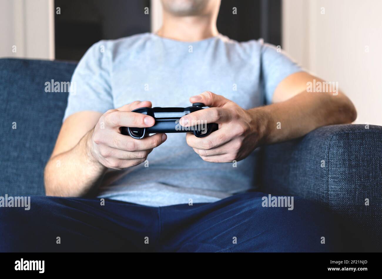 Video game controller in hand for console gaming. Gamer guy playing tv videogame with control gamepad or joystick while sitting home couch. Stock Photo