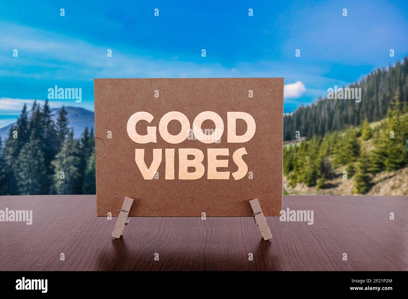 Good vibes text on card on the table with sunny summer mountains background. Stock Photo