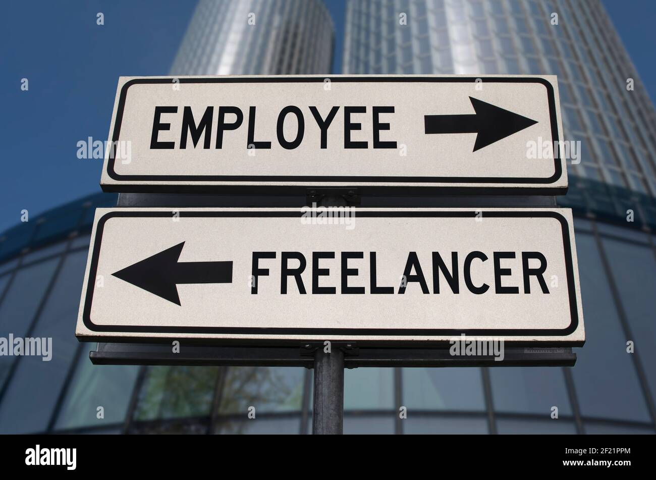 Employee versus freelancer road sign with two arrows on business skyscraper background. White two street sign with arrows on metal pole. Stock Photo