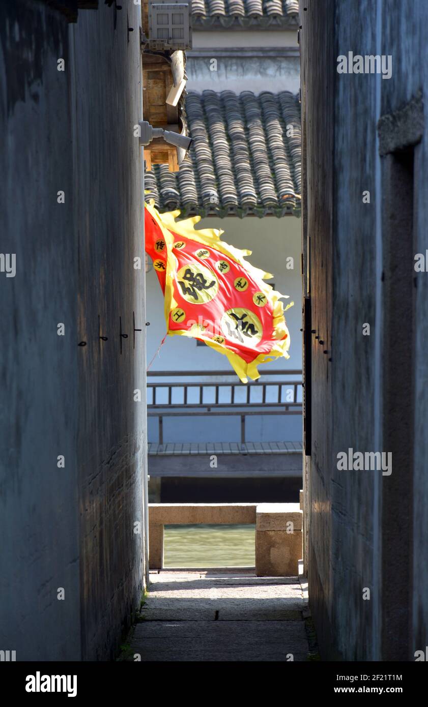 Bright red and yellow flag blows in the wind, breaking up the greys of the buildings and alleyway in this Chinese old town. Yuehe in Jiaxing. Stock Photo