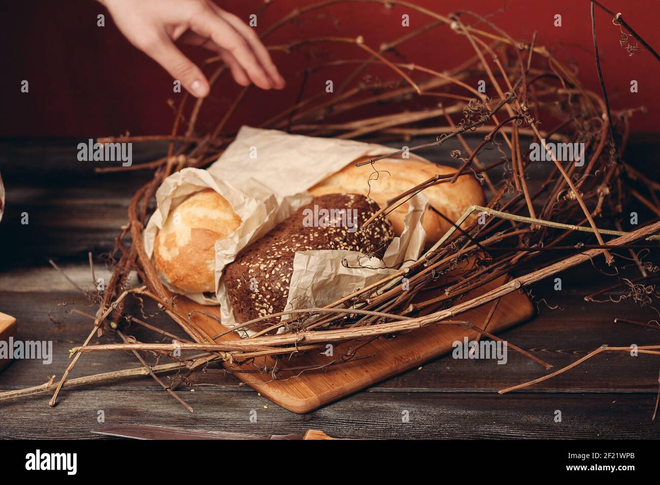 https://c8.alamy.com/comp/2F21WPB/a-loaf-of-bread-lies-on-the-branches-of-the-nest-on-a-wooden-table-on-a-red-background-2F21WPB.jpg
