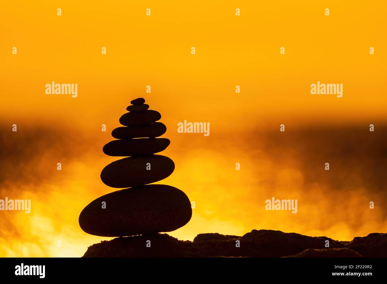 Balanced pebble pyramid silhouette on the beach. Abstract warm sunset bokeh with Sea on the background. Zen stones on the sea beach, meditation, spa Stock Photo