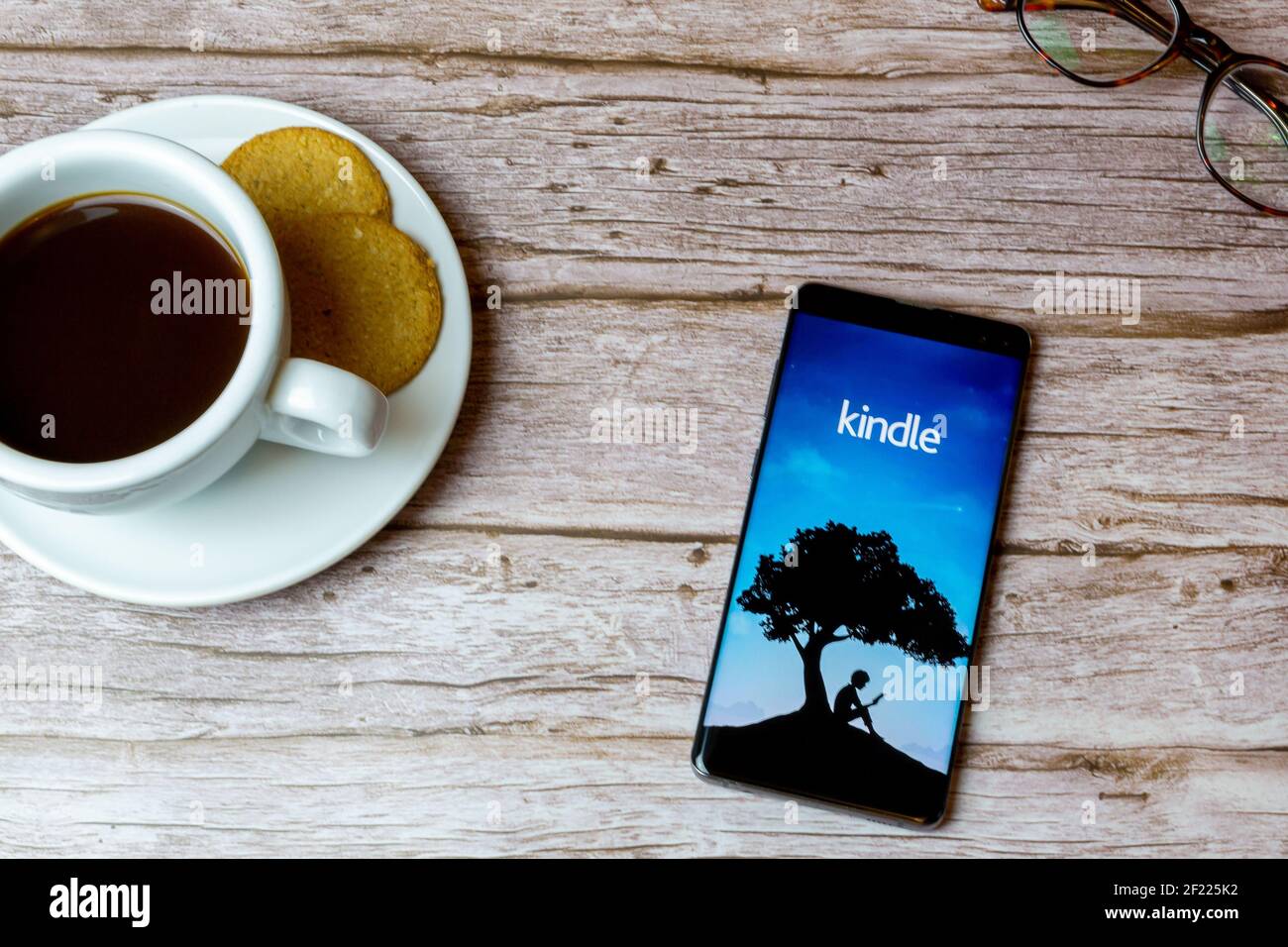 A Mobile phone or cell phone laid on a wooden table with the Amazon Kindle app opening also a coffee and glasses Stock Photo