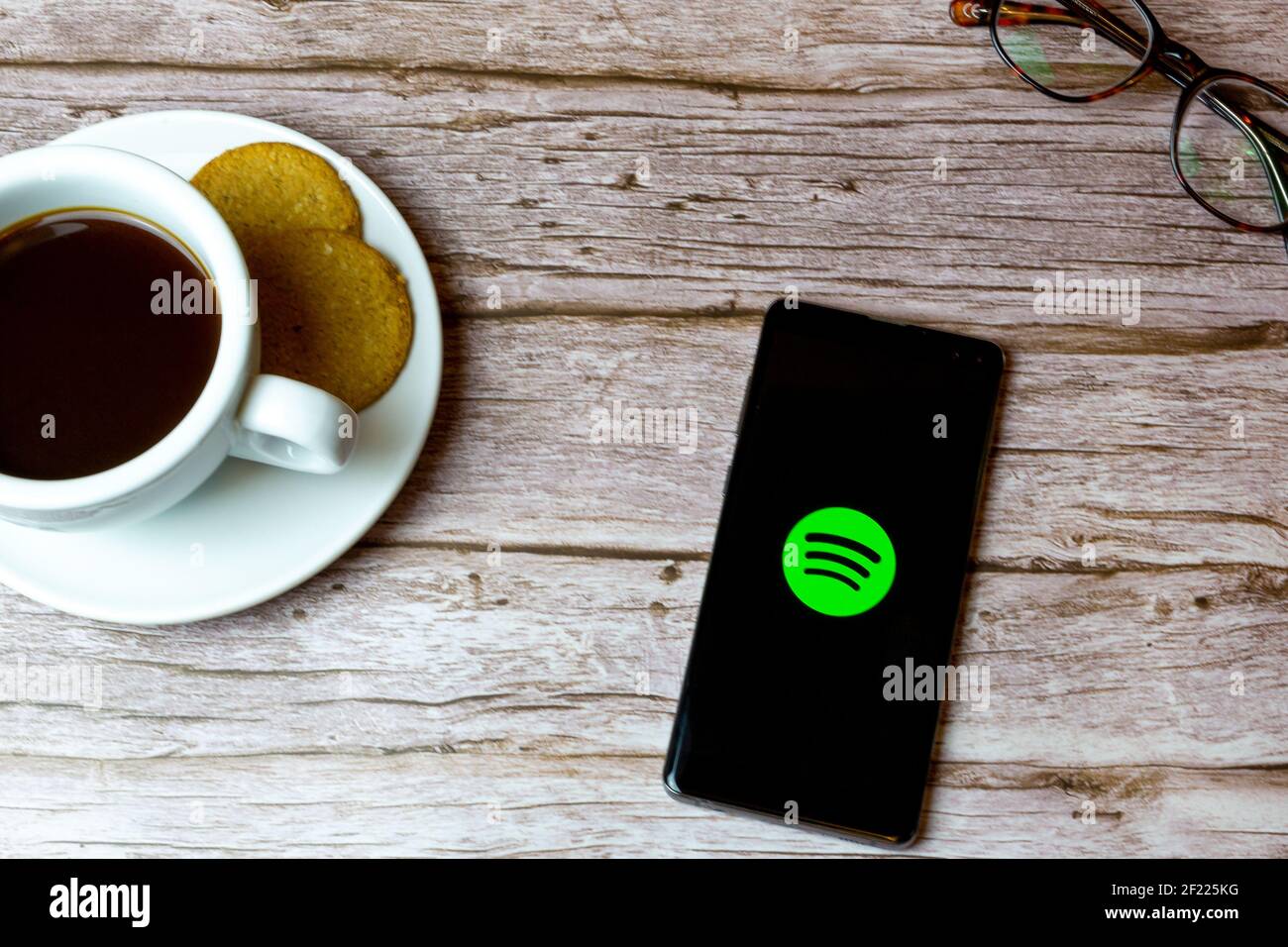 A Mobile phone or cell phone laid on a wooden table with the spotify app opening also a coffee and glasses Stock Photo