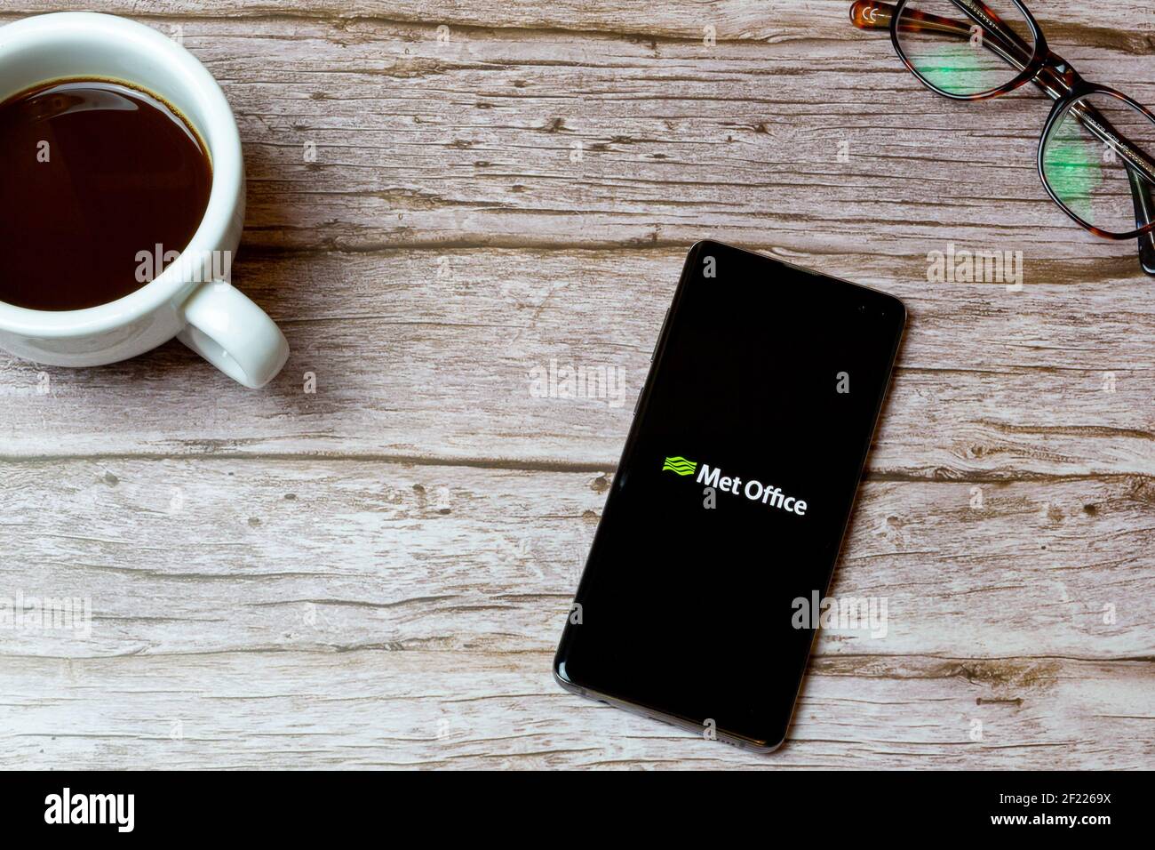 A Mobile phone or cell phone laid on a table or desk with the Met Office weather app open and a coffee next to it Stock Photo
