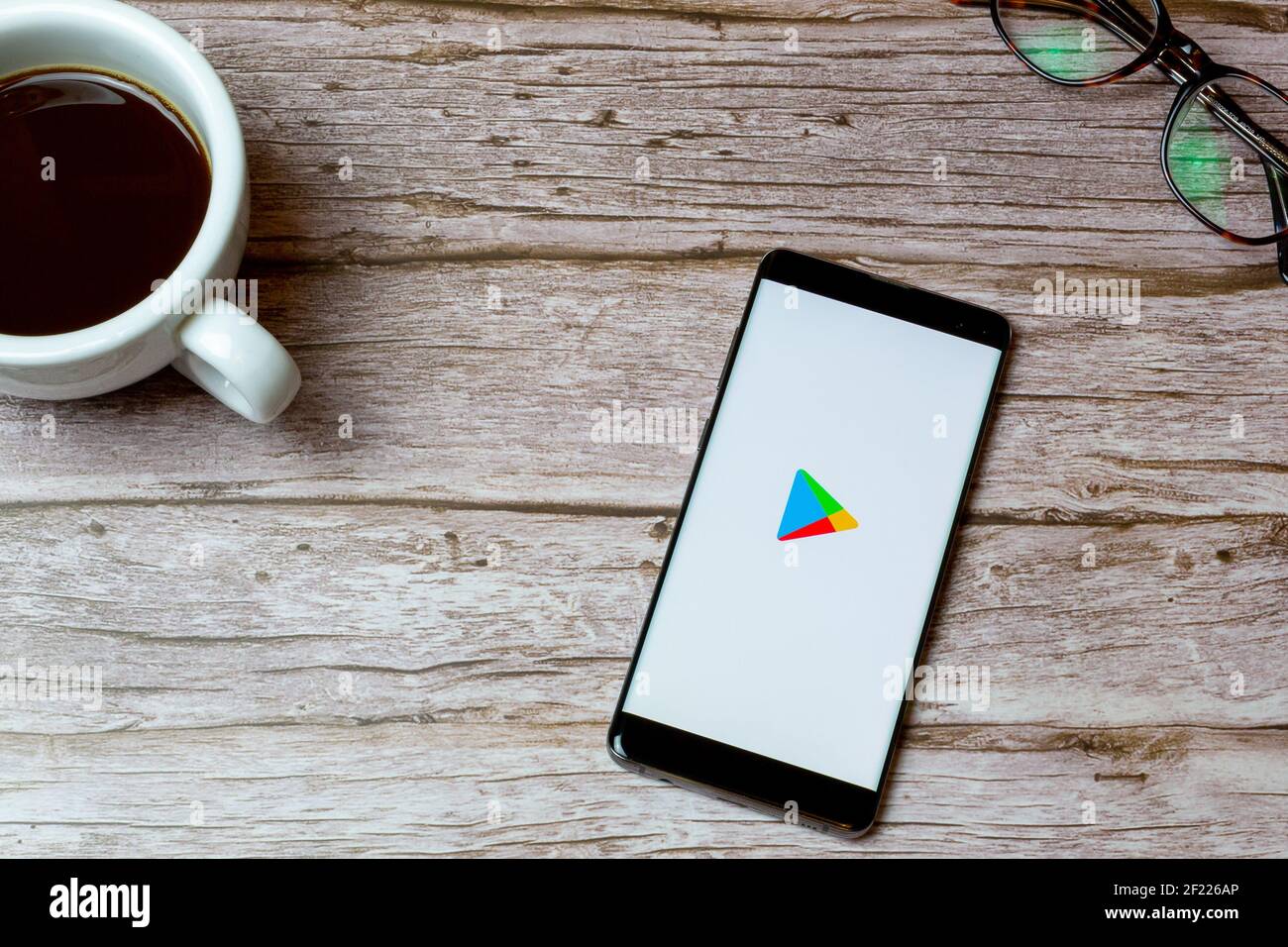 A Mobile phone or cell phone laid on a table or desk with the Google play store app open and a coffee next to it Stock Photo