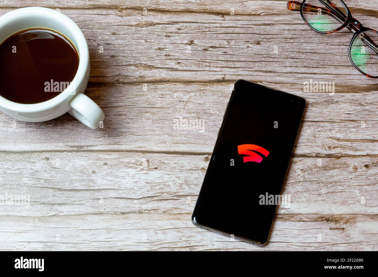 A Mobile phone or cell phone laid on a table or desk with the Google stadia app open and a coffee next to it Stock Photo