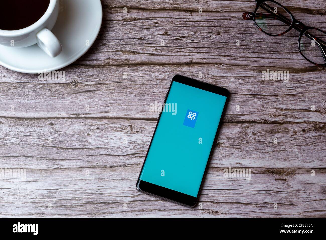 A mobile phone or cell phone laid on a wooden table or desk with the Co-Op app open Stock Photo