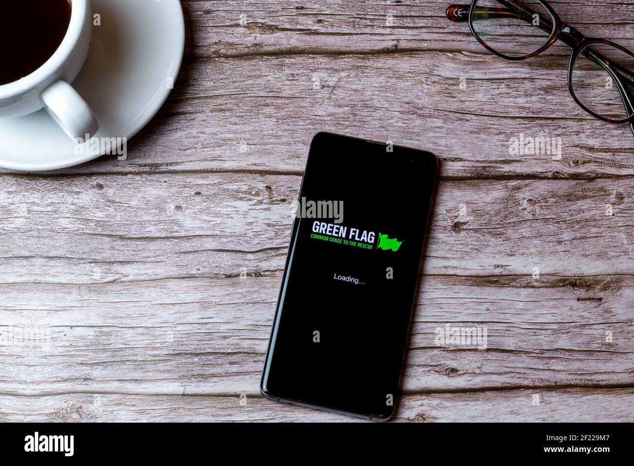 A mobile phone or cell phone laid on a wooden table with the Green Flag car breakdown app open next to a coffee Stock Photo