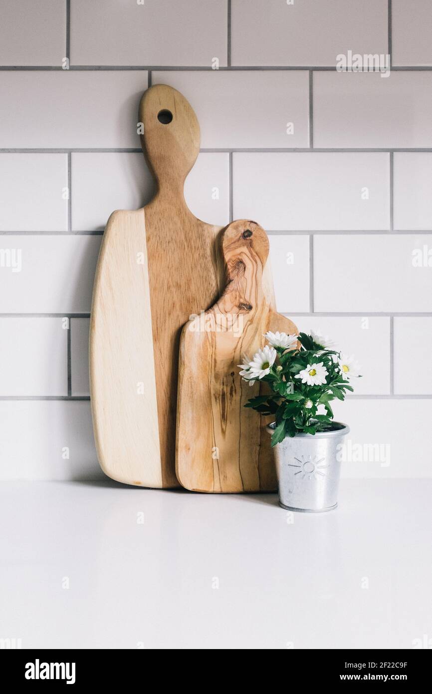 White daisies in a silver plant pot next to two wooden chopping boards leaning against white tiles in a kitchen Stock Photo