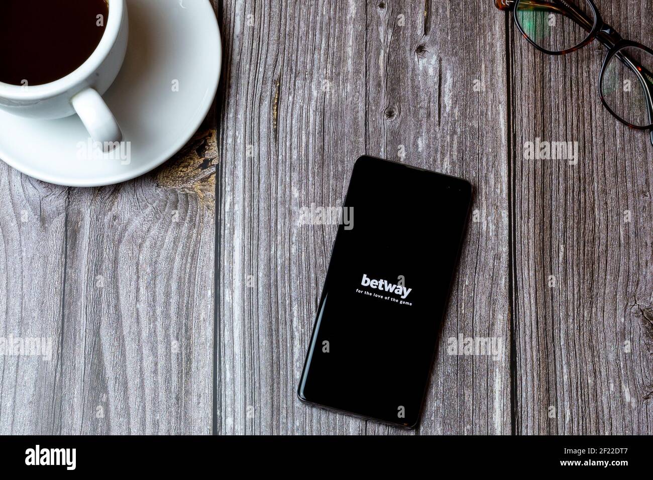 A mobile phone or cell phone laid on a wooden table with the Betway betting app open on screen next to a coffee Stock Photo
