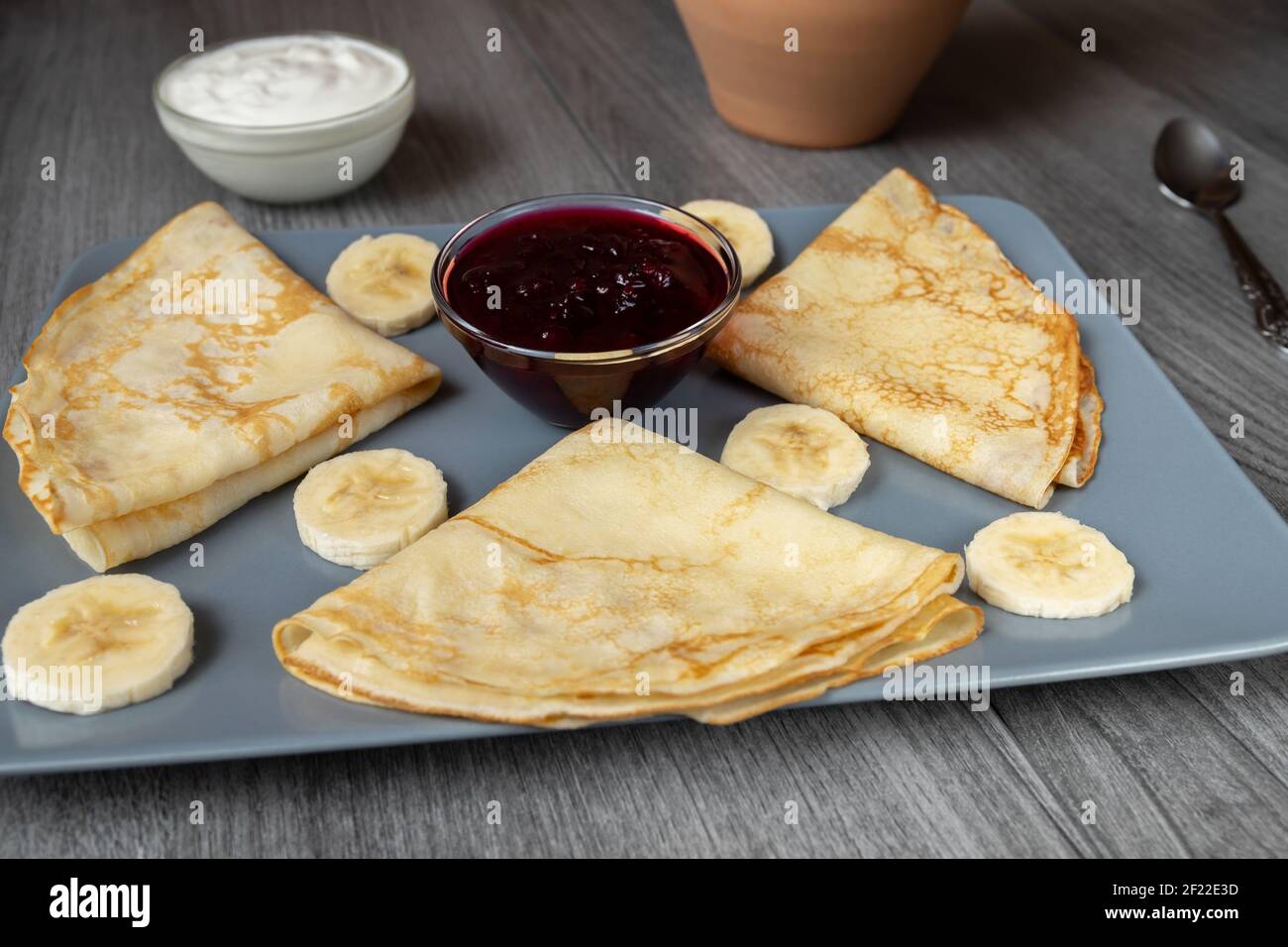 A portion of triangle-shaped pancakes on a gray-blue plate with banana, jam and sour cream Stock Photo