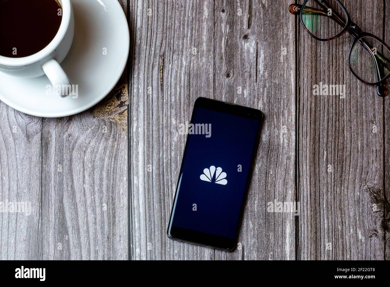 A mobile phone or cell phone laid on a wooden table with the NBC News app open on screen next to a coffee Stock Photo