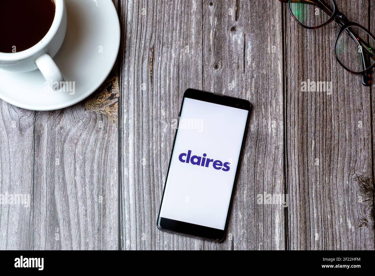 A mobile phone or cell phone laid on a wooden table with the claires app open on screen next to a coffee Stock Photo