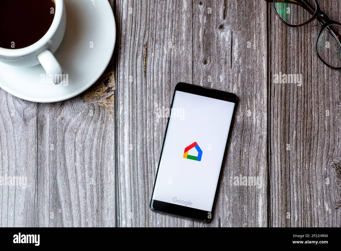 A mobile phone or cell phone laid on a wooden table with the Google home app open on screen next to a coffee Stock Photo