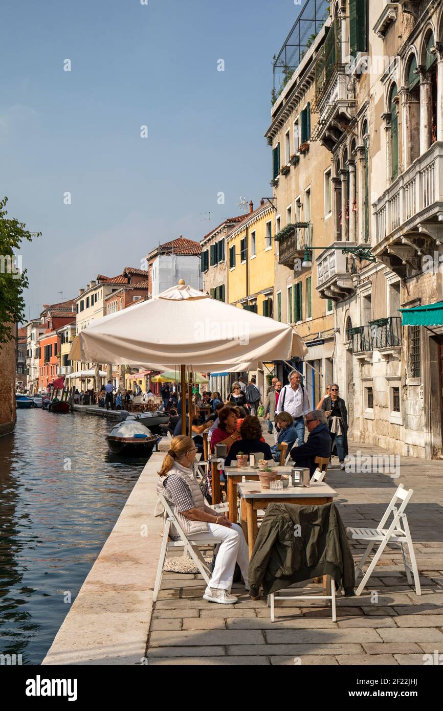 Tourists outside enjoying a meal at a restaurants along Fondamenta dei Ormisini beside Rio della Misericordia, Cannaregio, Venice, Italy Stock Photo