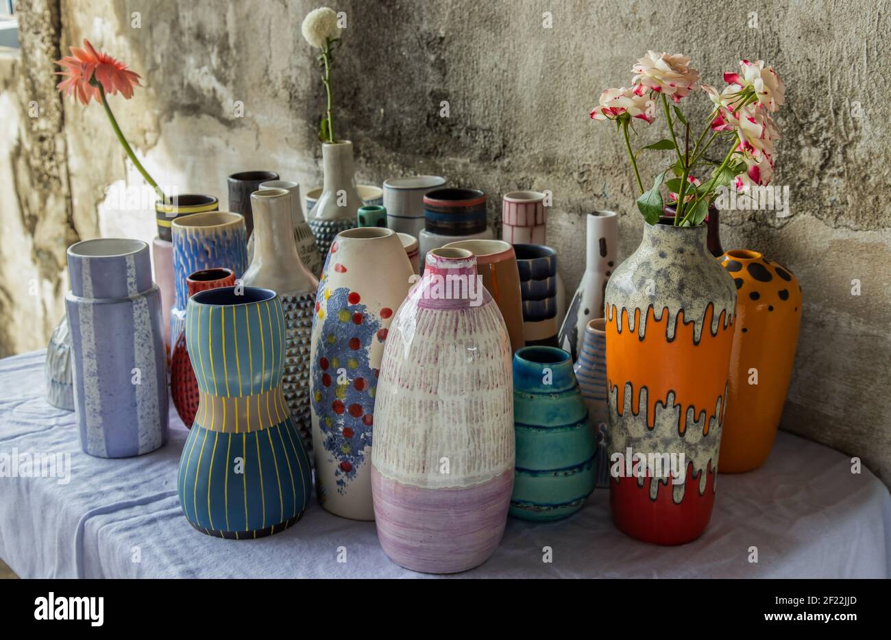 Bouquet of flowers in Handmade Assorted Many Different Ceramic Vases on Calico textured table cloth with old cement wall. Home decor. Selective focus. Stock Photo