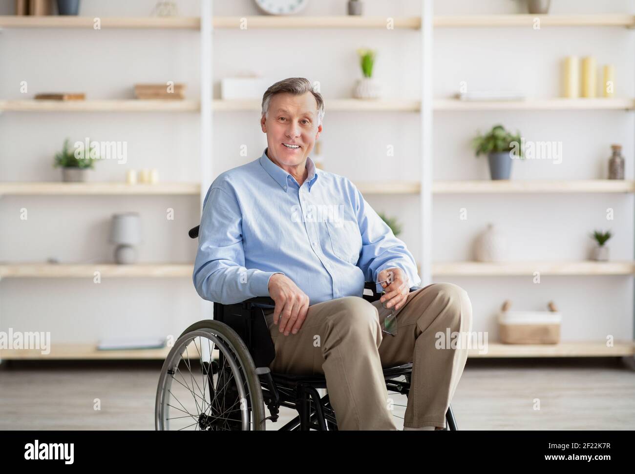 Joyful handicapped senior man in wheelchair smiling and looking at camera at retirement home Stock Photo