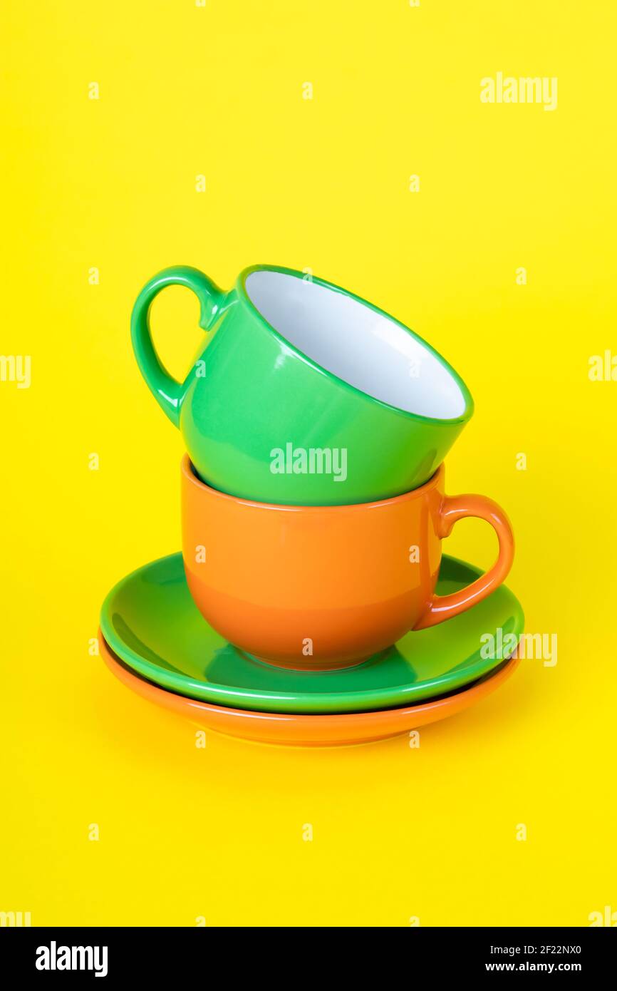 Two colorful empty tea cups and saucers. Typesetting dishes, a collection of coffee cups, a set of mugs. Ceramic painted utensils on a yellow backgrou Stock Photo