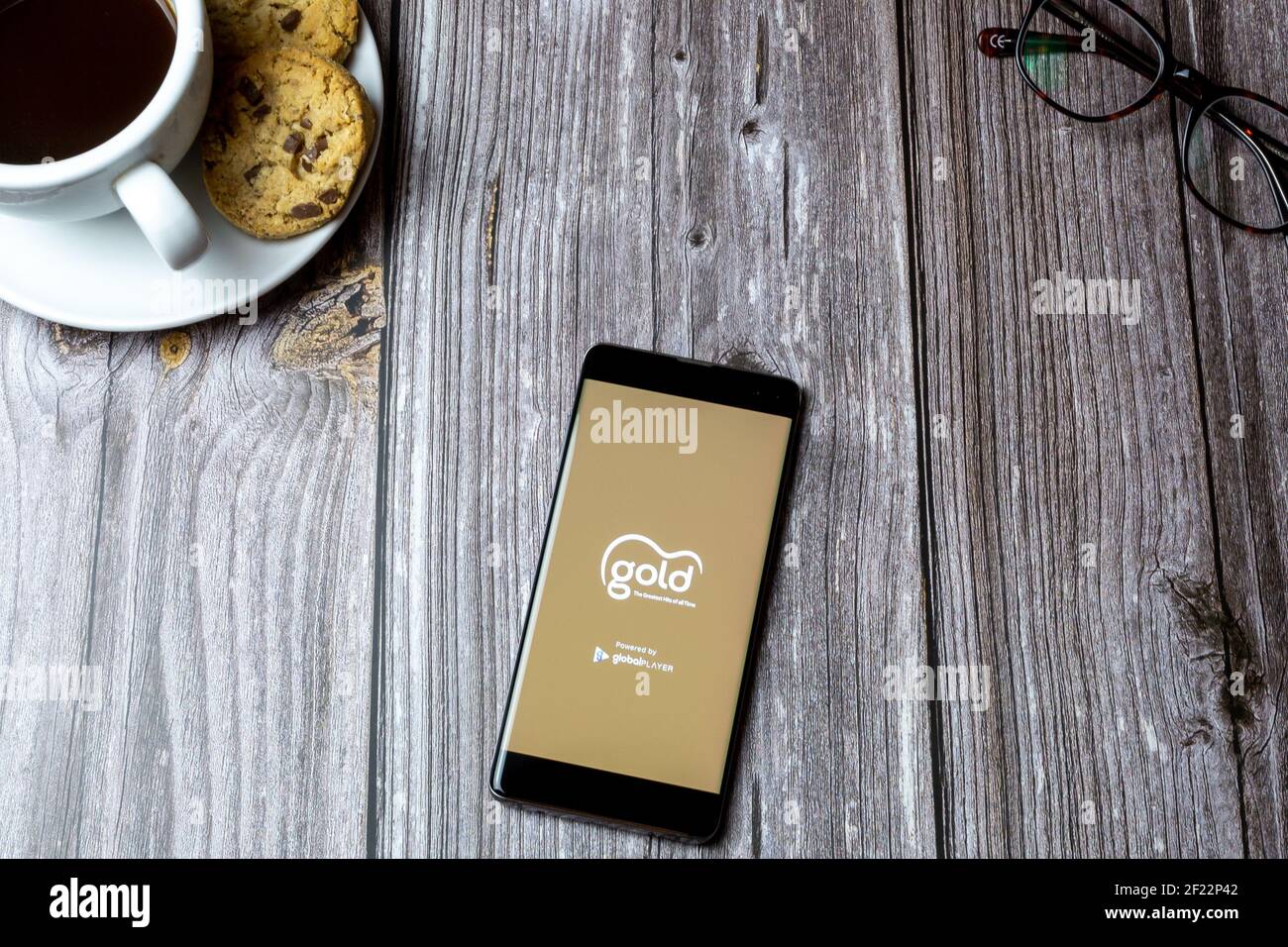 A mobile phone or cell phone laid on a wooden table with the Gold radio app open on screen Stock Photo