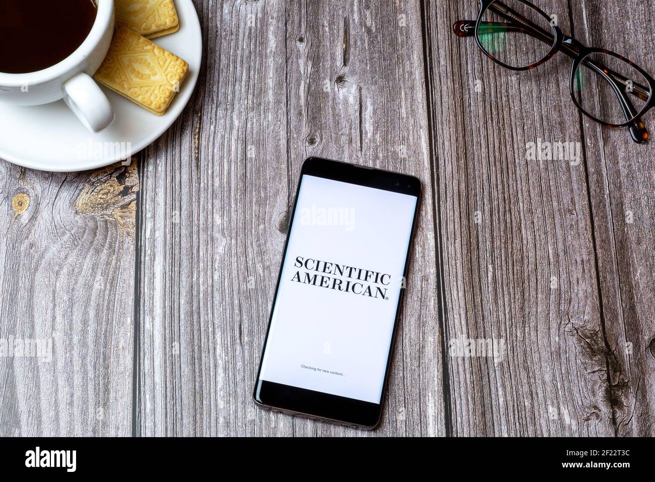 A mobile phone or cell phone on a wooden table with the Scientific American app open next to a coffee and glasses Stock Photo