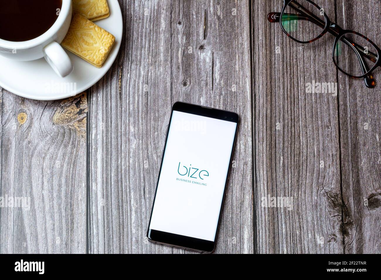 A mobile phone or cell phone on a wooden table with the Bize Business Emailing app open next to a coffee Stock Photo