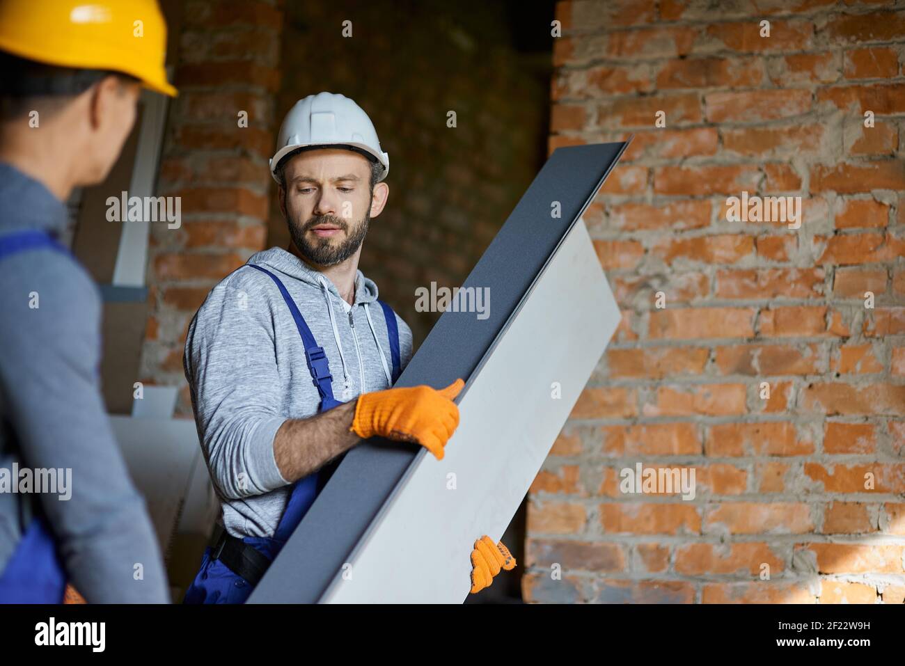 Confident young male builders wearing hard hats looking focused, holding metal stud for drywall while working together at construction site. Building house, profession, teamwork concept Stock Photo