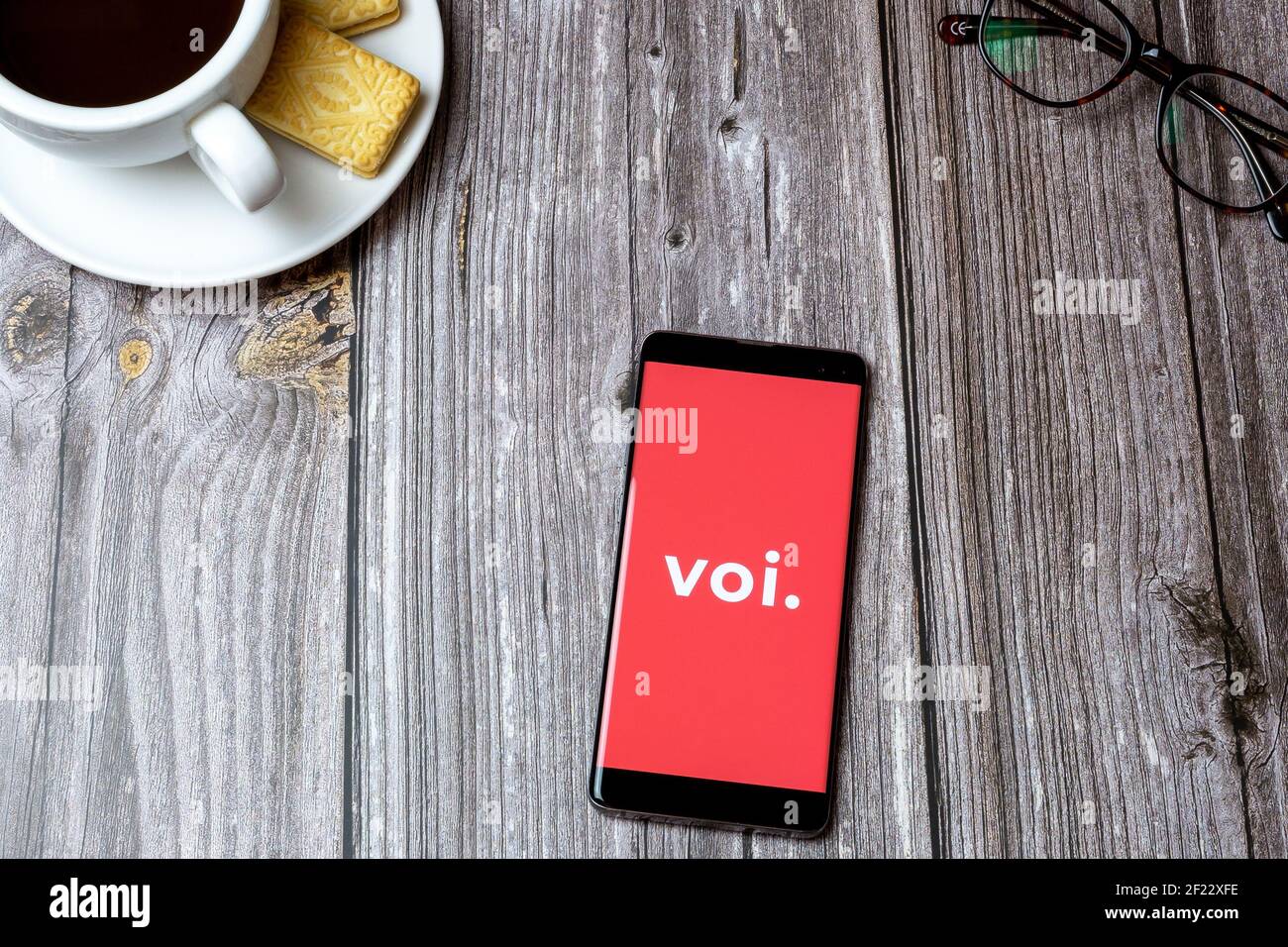 A mobile phone or cell phone on a wooden table with the VOI scooters app open next to a coffee and glasses Stock Photo