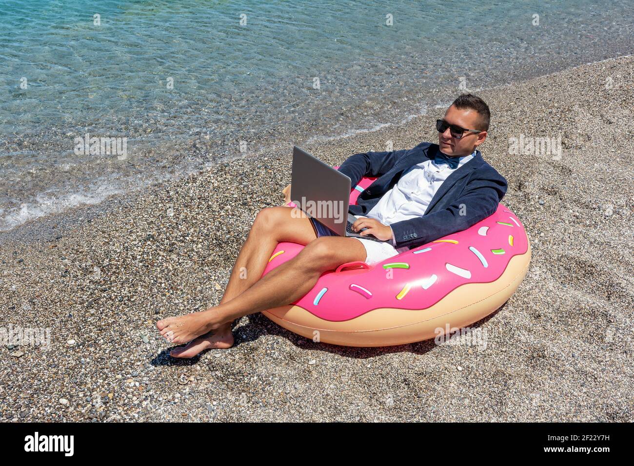 Businessman using laptop computer on inflatable donut on tropical beach ...
