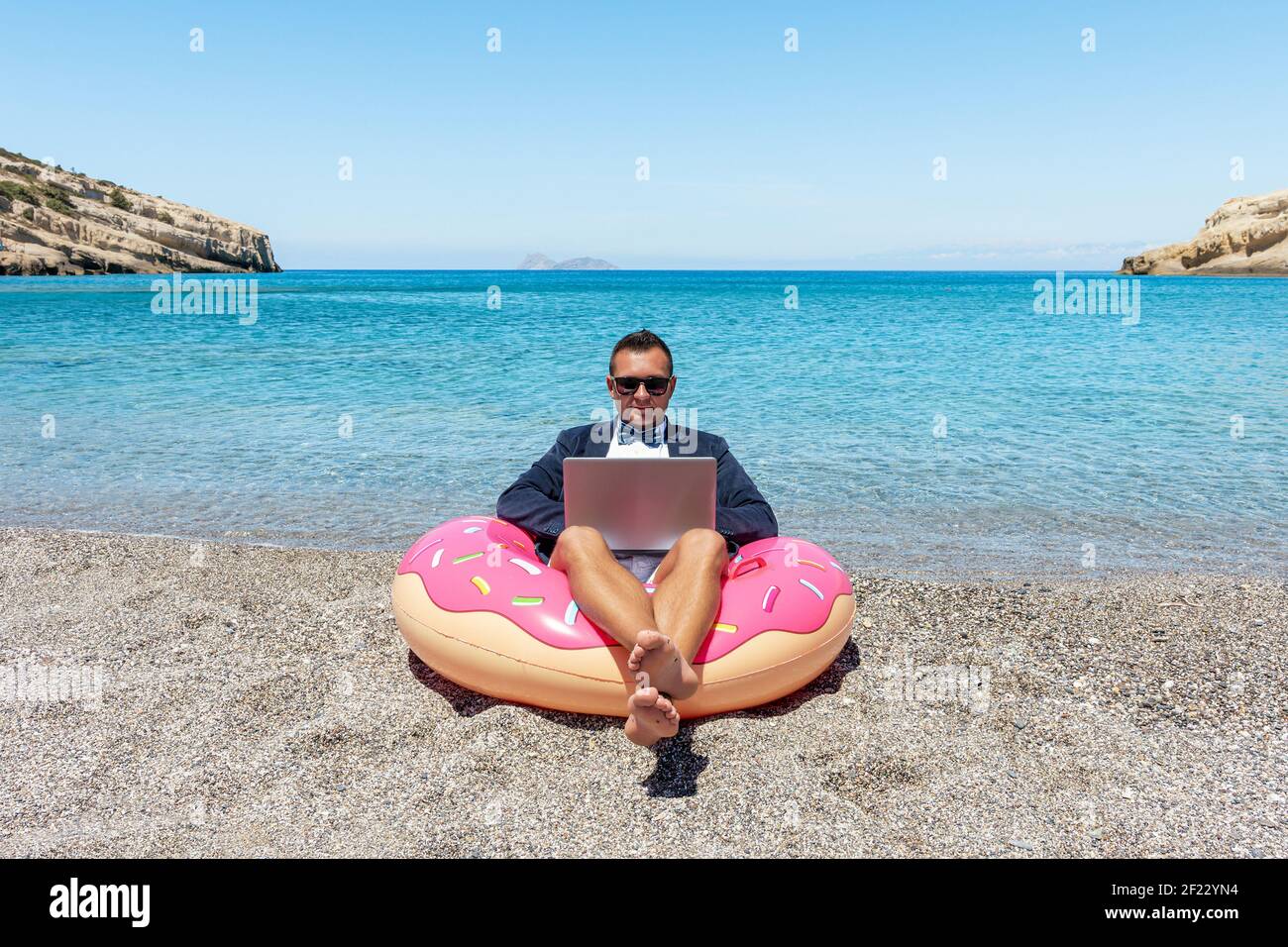 Businessman using laptop computer on inflatable donut on tropical beach ...