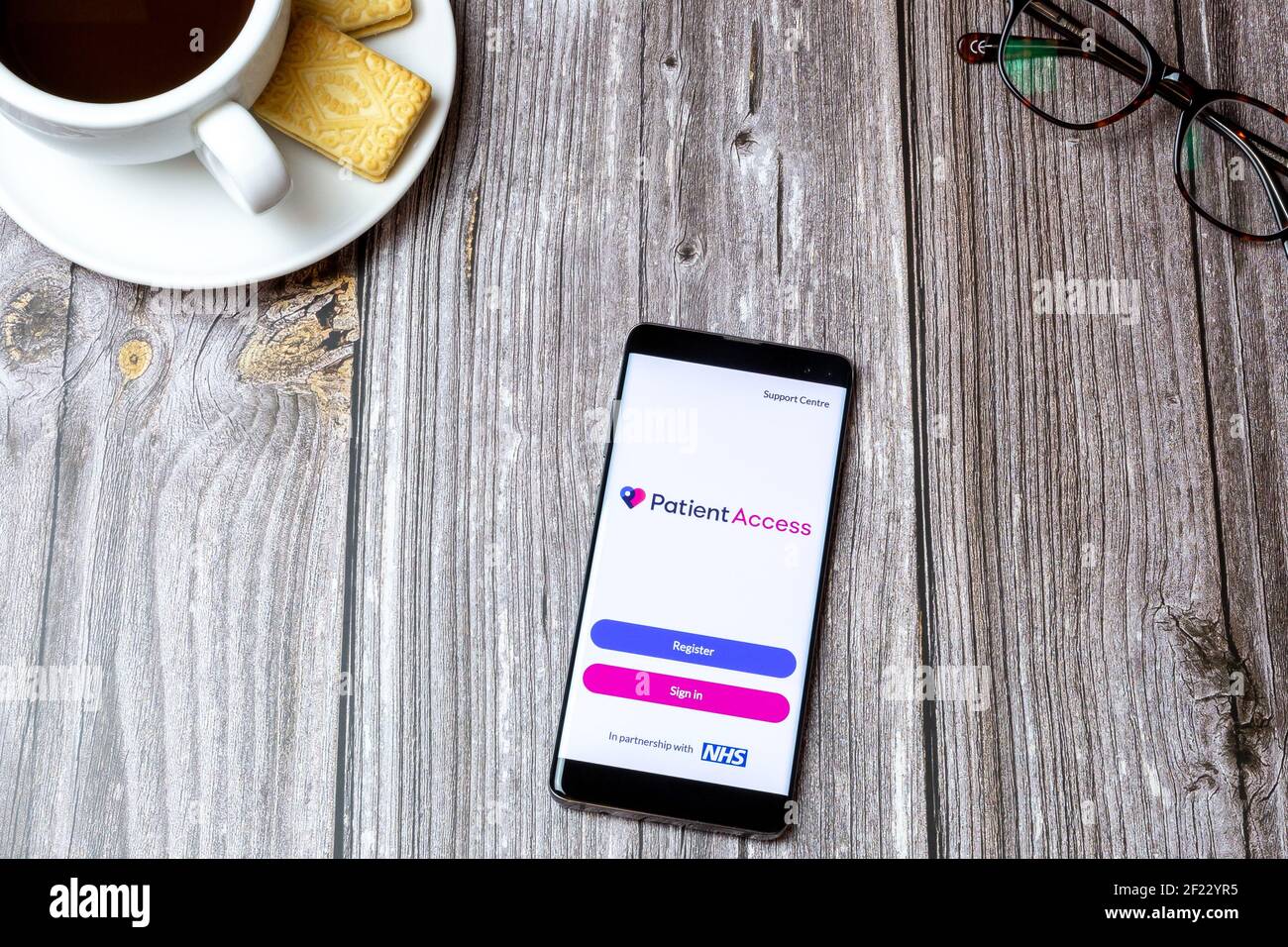 A Mobile Phone Or Cell Phone On A Wooden Table With The Patient Access App Open Next To A Coffee And Glasses Stock Photo Alamy