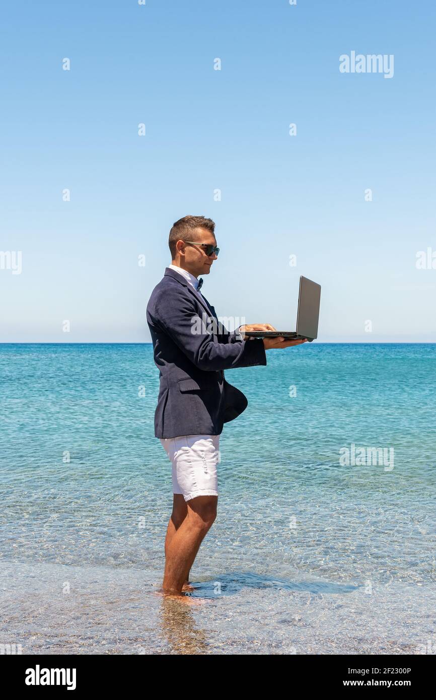 Businessman using laptop computer on tropical beach. Summer vacation concept. Stock Photo