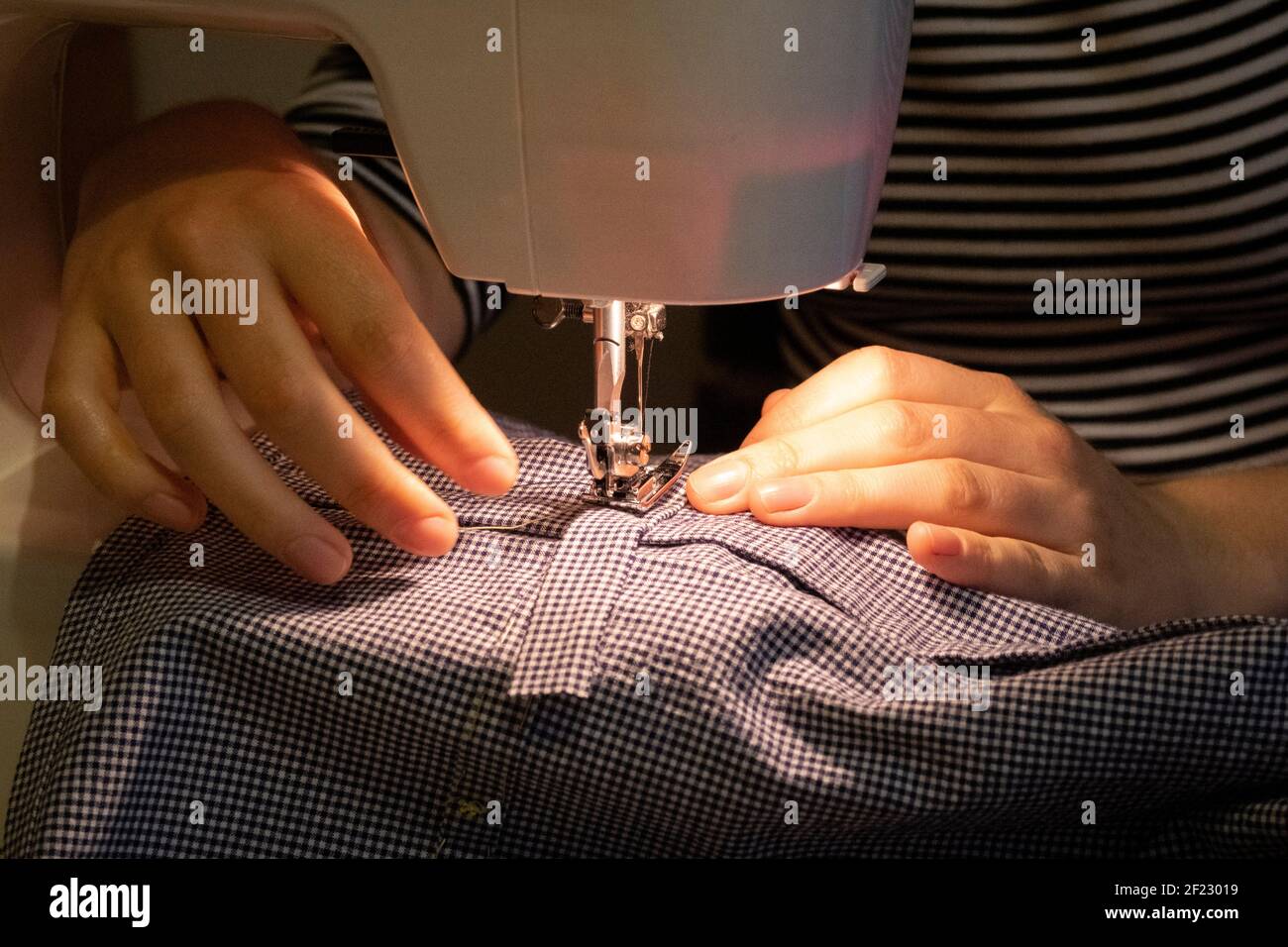Using her own sewing machine, a young dressmaking hobbyist woman sews together the seams of a home-made dress that she's created from a pattern in her home, on 6th March 2021, in London, England. Stock Photo