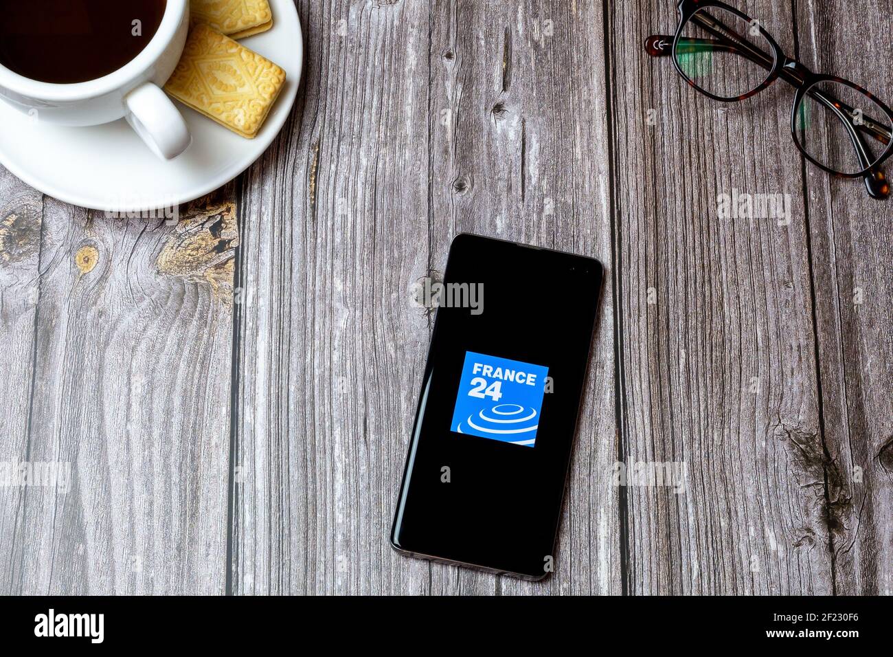 A mobile phone or cell phone on a wooden table with the France 24 news app open next to a coffee and glasses Stock Photo