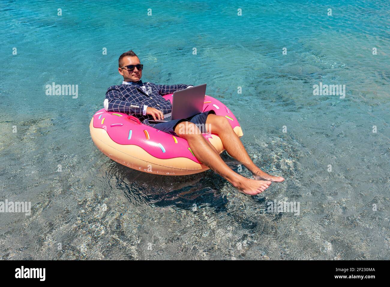 Businessman using laptop computer on an inflatable donut in the sea ...