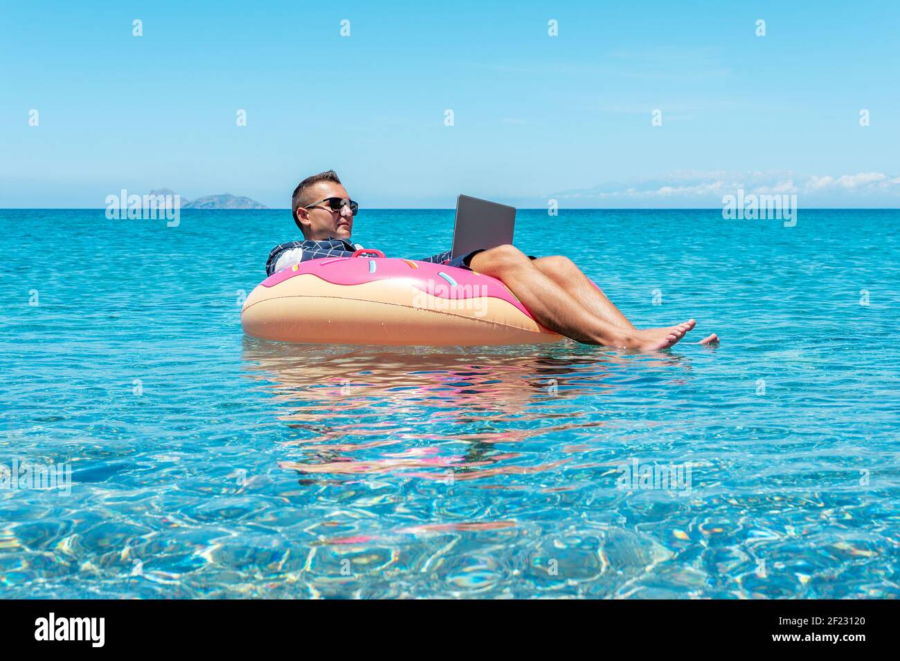 Businessman using laptop computer on an inflatable donut in the sea ...