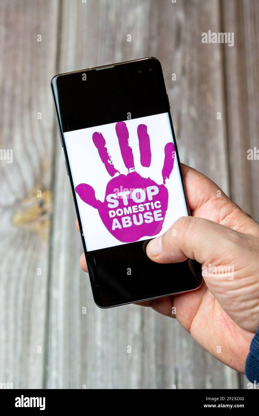 A Mobile phone or cell phone being held in a hand with the stop domestic abuse logo open on screen Stock Photo