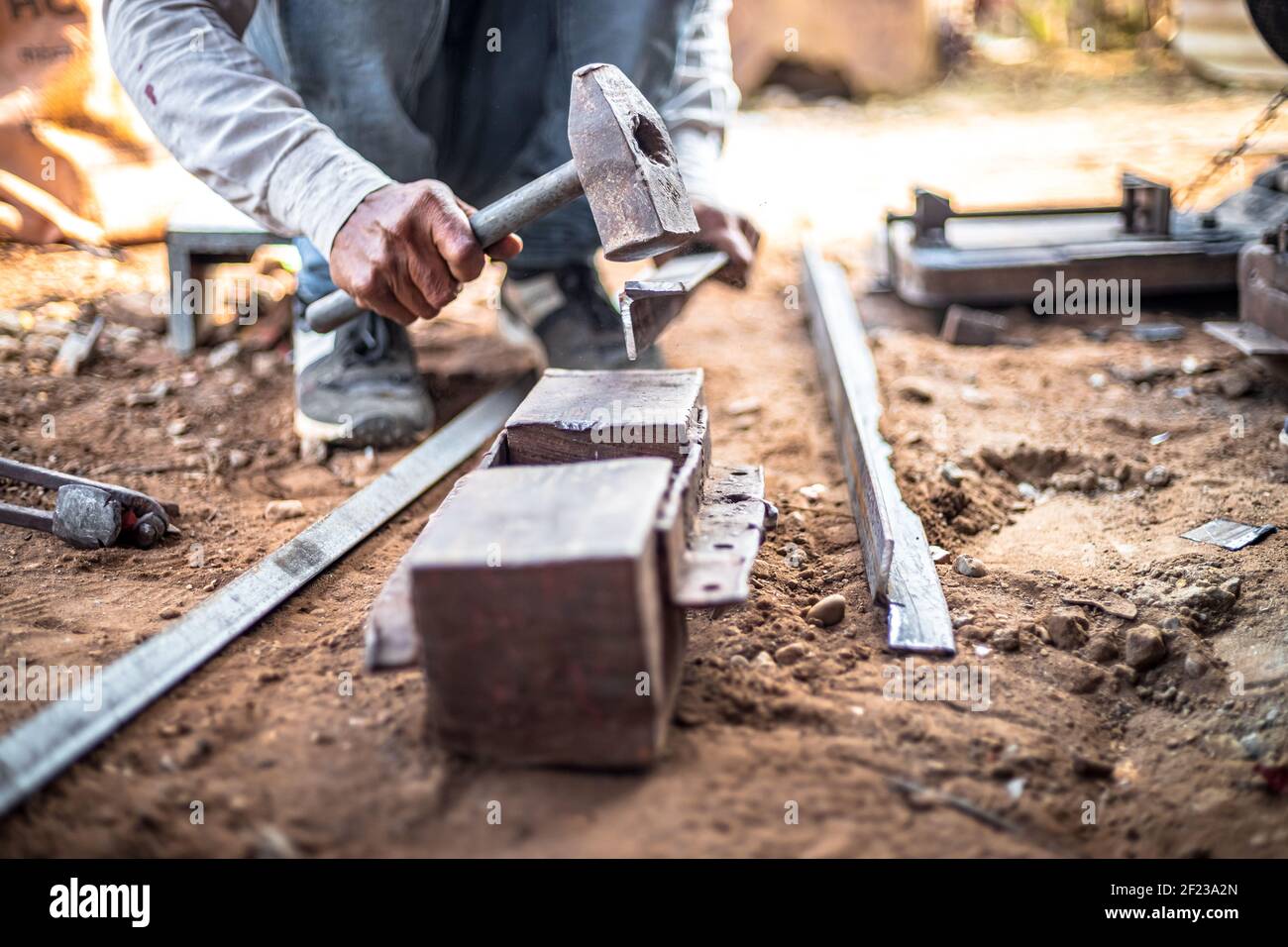 Closeup hands of a blacksmith hits iron or steel sheet with a hammer at a workshop outdoors. Stock Photo