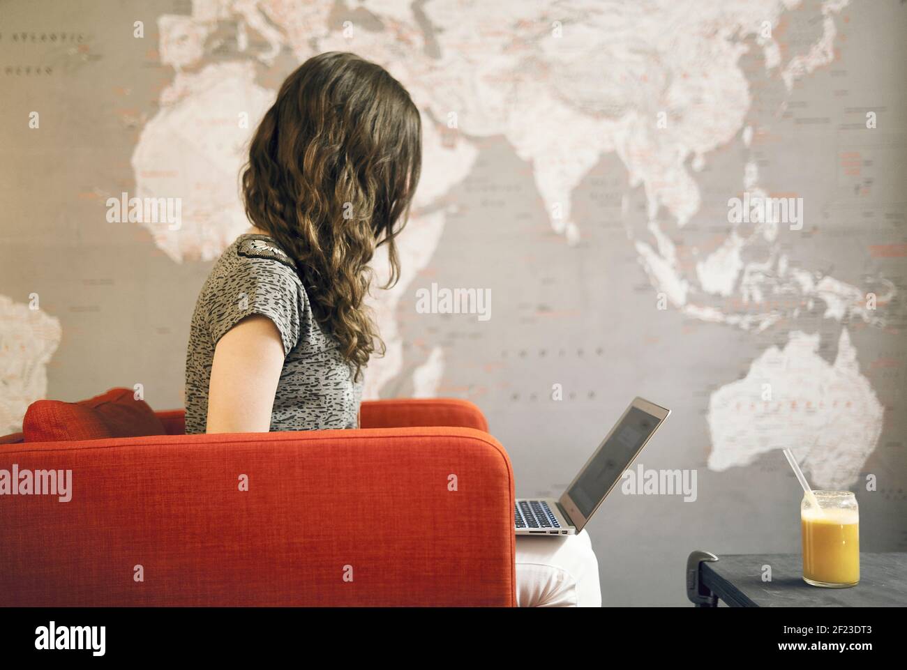 Close-up of young female on laptop with world map on the wall. Digital nomad, remote working, blogger or travel hacking concept Stock Photo
