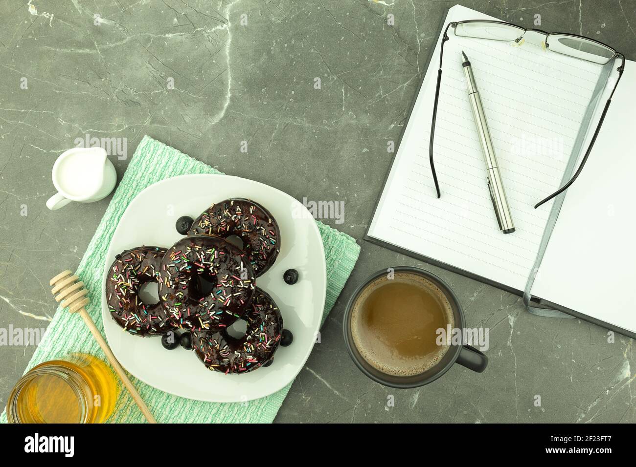 Round donut in chocolate on a white plate. Fresh donut and coffee on the table. Space for text Stock Photo
