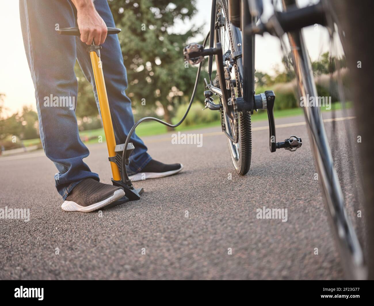 Cropped shot of young man using pump while inflating the tire of his bicycle, standing in public park on a daytime. Transportration, healthy lifestyle concept Stock Photo